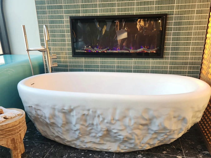 fre standing textured bathtub in fron of a gas wall fireplace